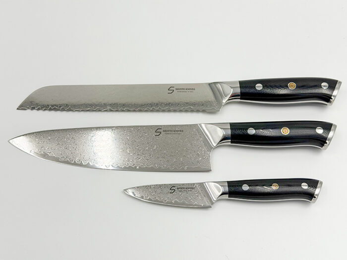 Shinto knivsæt i damaskusstål med kokkekniv, brødkniv og urtekniv på køkkenbord
